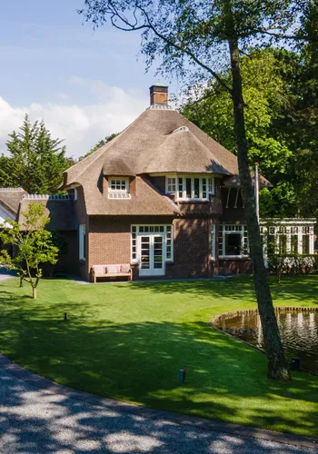 een modern huis met een riet dak en een garage met een vijver